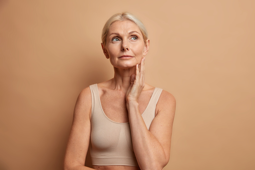 woman-touches-skin-after-applying-anti-age-cream-concentrated-with-thoughtful-expression-wears-cropped-top-isolated-brown